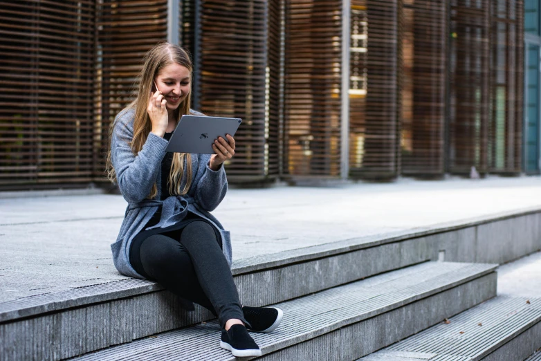 a woman sitting on steps using a tablet computer, pexels contest winner, post graduate, looking partly to the left, all around, student