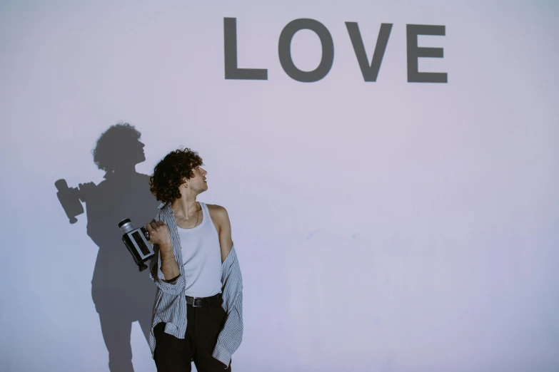 a man standing in front of a wall with the word love written on it, an album cover, pexels contest winner, robert sheehan, carrying a bottle of perfume, woman love woman, lesbians