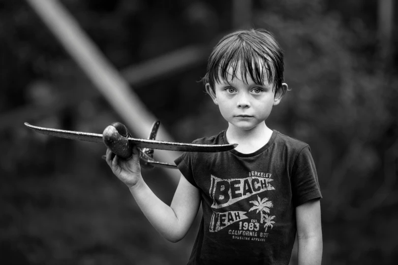 a black and white photo of a young boy holding a sword, by Adam Marczyński, pexels contest winner, realism, girl with warship parts, adventure playground, holding a ray gun, portrait of small