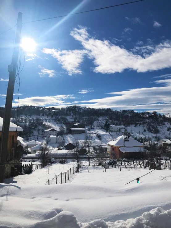 a person riding skis down a snow covered slope, by Muggur, happening, quaint village, sunny at noon, 💋 💄 👠 👗, bosnian