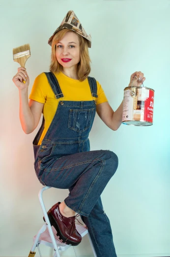 a woman sitting on a ladder holding a paintbrush and a paint can, pexels contest winner, wearing overalls, gold paint, gif, indoor picture