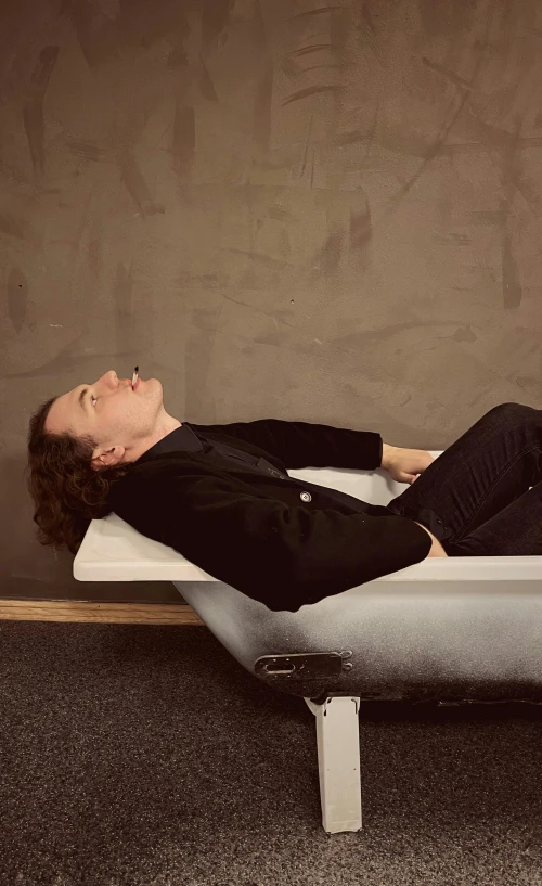 a person laying on a bed in a room, an album cover, inspired by Sarah Lucas, unsplash, tommy wiseau, bathtub, 15081959 21121991 01012000 4k, in a black suit