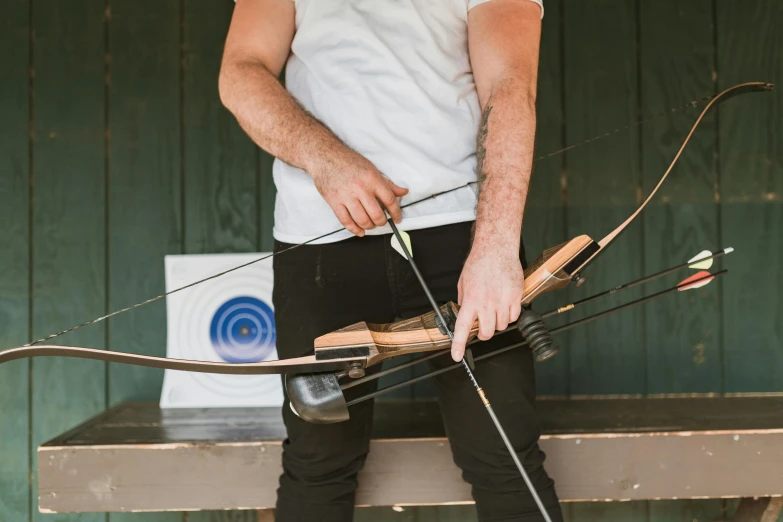 a man standing on a bench holding a bow and arrow, pexels contest winner, upper body close up, lachlan bailey, casual game, top-down shot