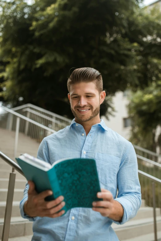 a man in a blue shirt is reading a book, smiling with confidence, post graduate, 2019 trending photo, walking down