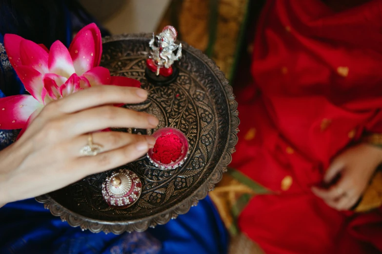 a close up of a person holding a plate with rings on it, pexels contest winner, hurufiyya, red brocade and blue gemstones, hindu gods, holding flowers, thumbnail