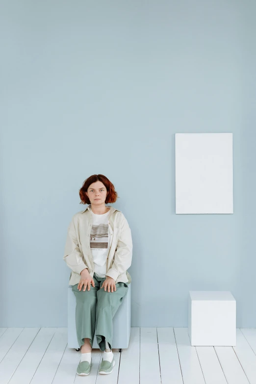 a woman sitting on a chair in front of a blue wall, a minimalist painting, by Attila Meszlenyi, visual art, sadie sink, in a white room, in an art gallery], plain background