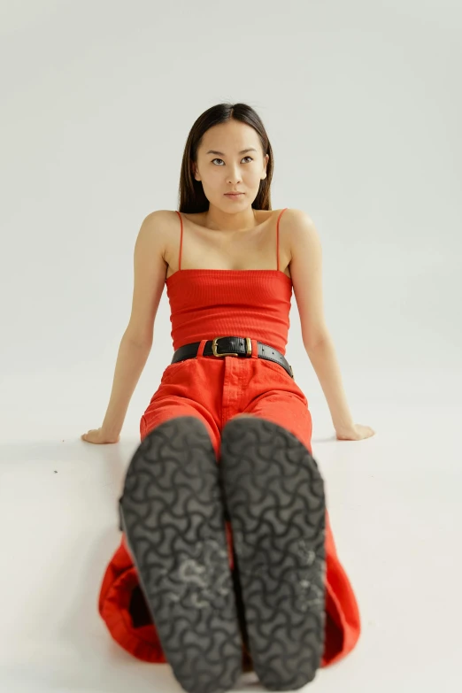 a woman in a red dress is sitting on the floor, an album cover, inspired by Feng Zhu, trending on pexels, wearing overalls, intimidating pose, on a white table, wearing a camisole and boots