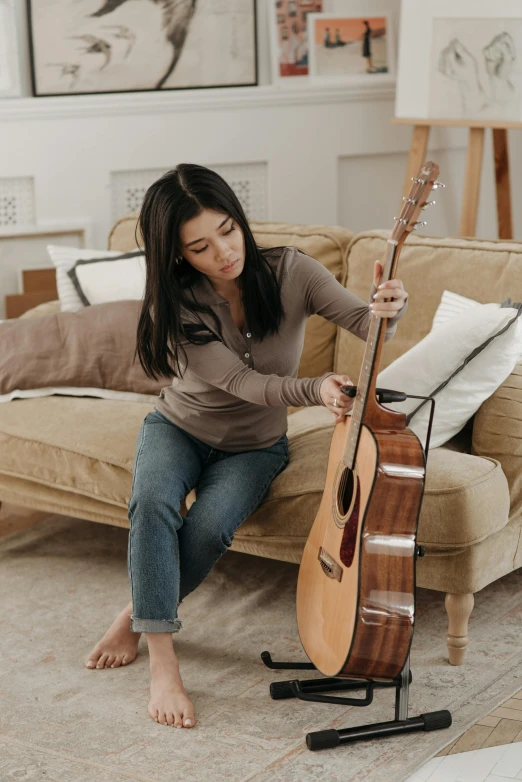 a woman sitting on a couch playing a guitar, inspired by Ruth Jên, pexels contest winner, joanna gaines, mai anh tran, pulling strings, comfort