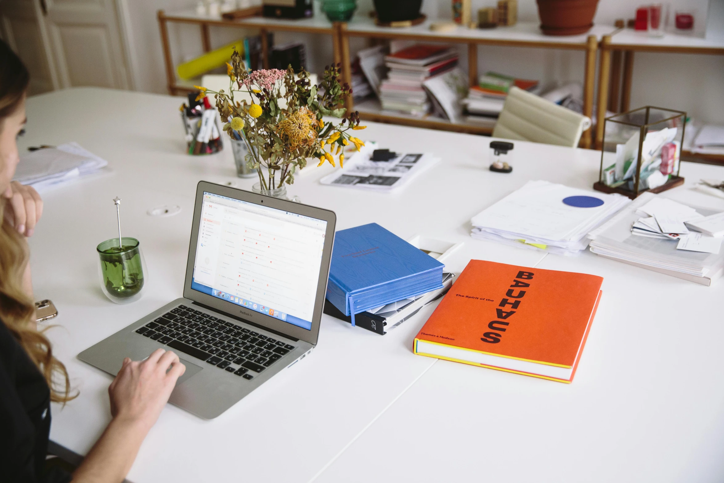 a woman sitting at a table with a laptop computer, an album cover, unsplash, arbeitsrat für kunst, in an office, 9 9 designs, swedish writing, stack of books on side table