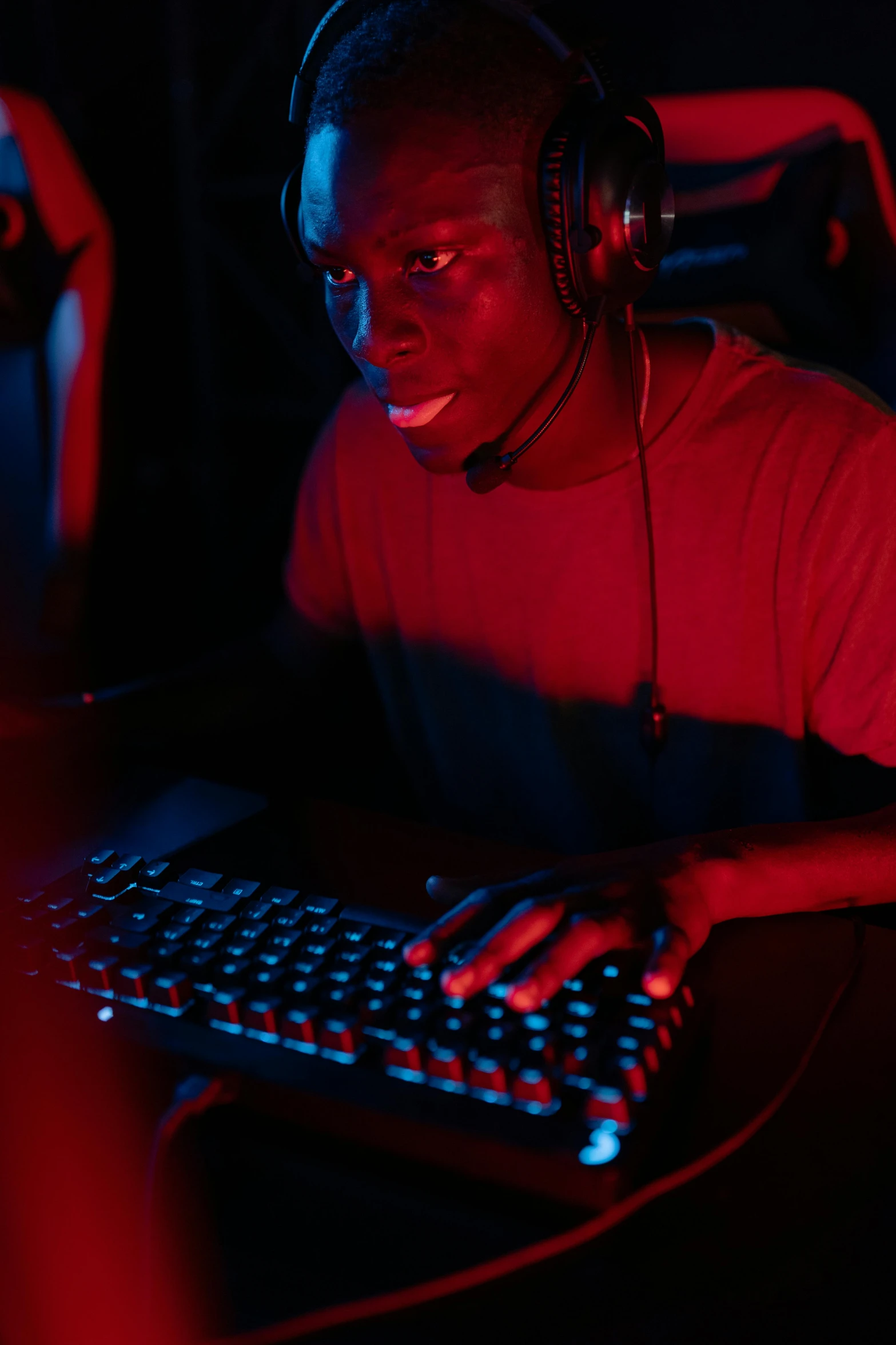 a man wearing headphones sitting in front of a computer, led gamers keyboard, ( ( dark skin ) ), red colored, tournament