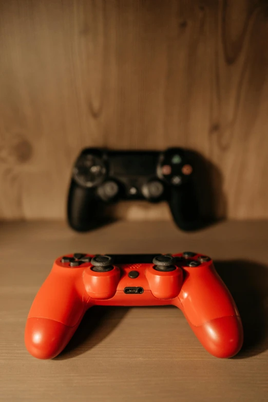 a couple of video game controllers sitting on top of a wooden table, red and orange colored, taken with sony alpha 9, image, game