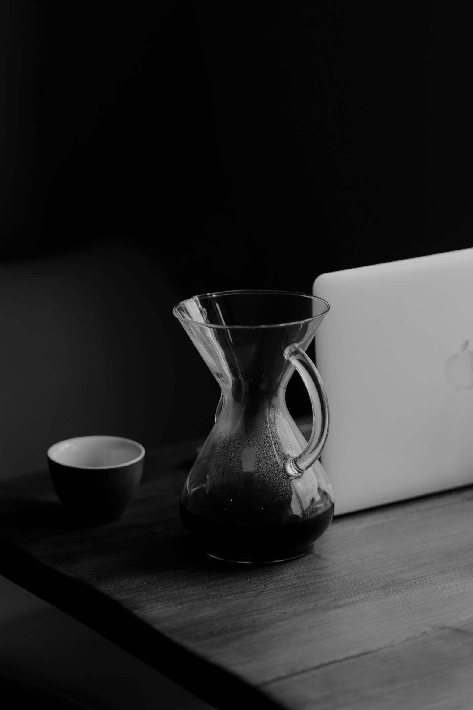 a laptop computer sitting on top of a wooden table, a black and white photo, by Cafer Bater, unsplash, minimalism, vessels, pouring, late morning, a horned