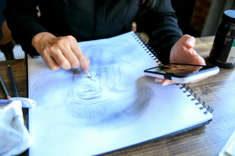 a woman sitting at a table drawing on a piece of paper, a drawing, by Julia Pishtar, trending on pexels, interactive art, airbrush painting, holding notebook, dissection sketch, full device