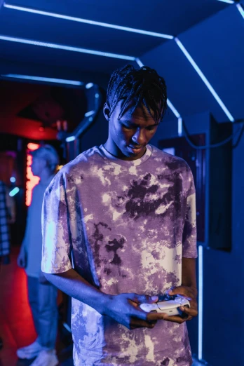 a man standing in a room holding a cell phone, an album cover, trending on pexels, holography, purple clothes, night clubs and neons, black teenage boy, drippy