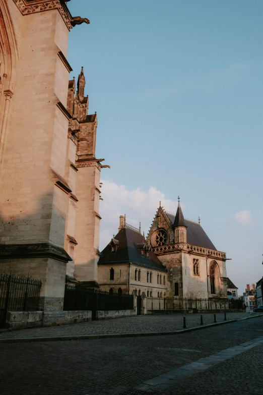 a man riding a skateboard down a street next to a tall building, a picture, by Raphaël Collin, unsplash, baroque, behind her a gothic cathedral, french village exterior, early morning light, square