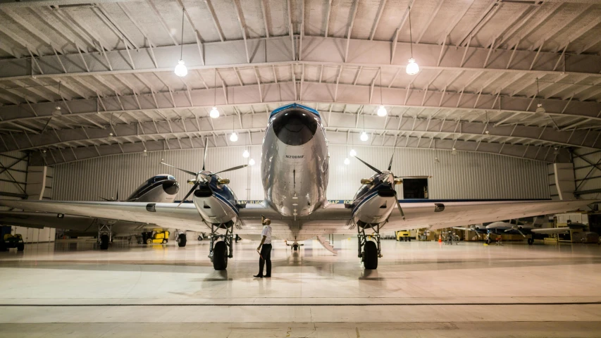 a man standing in front of an airplane in a hangar, by Ben Zoeller, unsplash, photorealism, symmetrical front view, airplanes, retro style ”, large scale photo