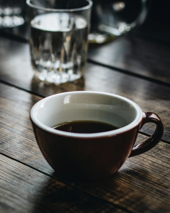 a cup of coffee sitting on top of a wooden table, next to a cup, uncropped, multiple stories, glassware