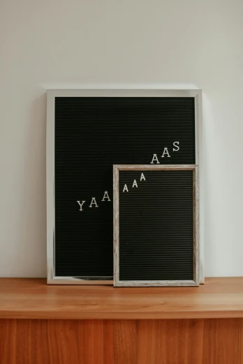 a couple of framed letters sitting on top of a wooden shelf, by Adam Rex, unsplash contest winner, yawning, black vertical slatted timber, say ahh, whiteboards