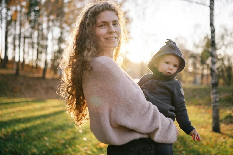 a woman holding a baby in her arms, by Emma Andijewska, pexels contest winner, of a family standing in a park, soft light.4k, thumbnail