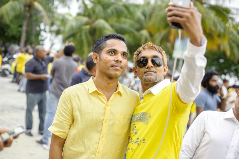 a couple of men standing next to each other on a beach, a picture, happening, audience selfie, sri lanka, yellow theme, avatar image