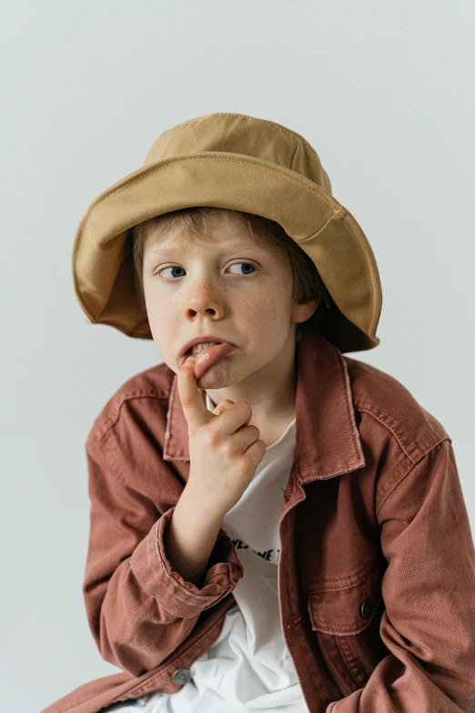 a little boy sitting on a stool with a hat on, inspired by Joseph Beuys, pexels, light tan, wearing jacket, manuka, ( 3 1