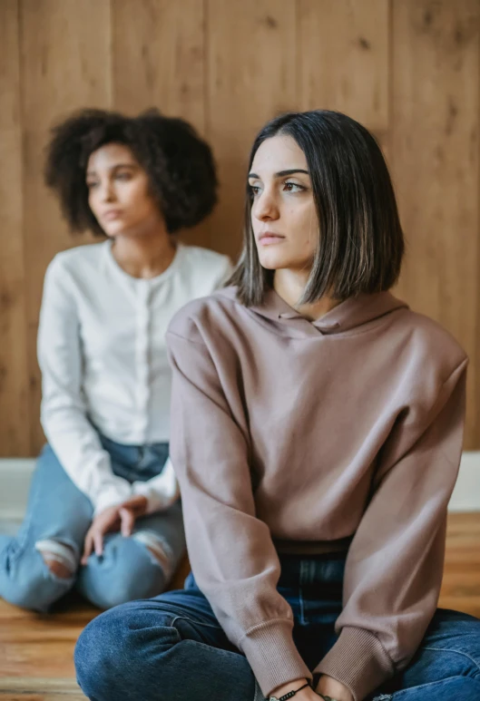 two women sitting on the floor in front of a wooden wall, by Adam Marczyński, trending on pexels, renaissance, depressed sad expression, wearing a white sweater, focus her back, sitting in a waiting room