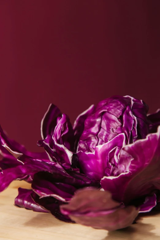 a purple flower sitting on top of a wooden table, the anatomy of a head of lettuce, on a sumptuous velvet tablecloth, zoomed in, crimson themed