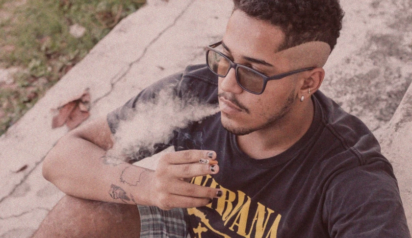 a man sitting on a curb smoking a cigarette, an album cover, trending on pexels, portrait of danny gonzalez, wearing shades, nug pic, sunfaded