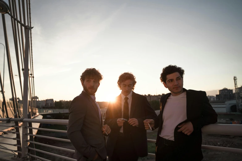 three men standing next to each other on a bridge, an album cover, by Niko Henrichon, pexels contest winner, renaissance, sun down golden hour, wearing a suits, luca, rooftop party