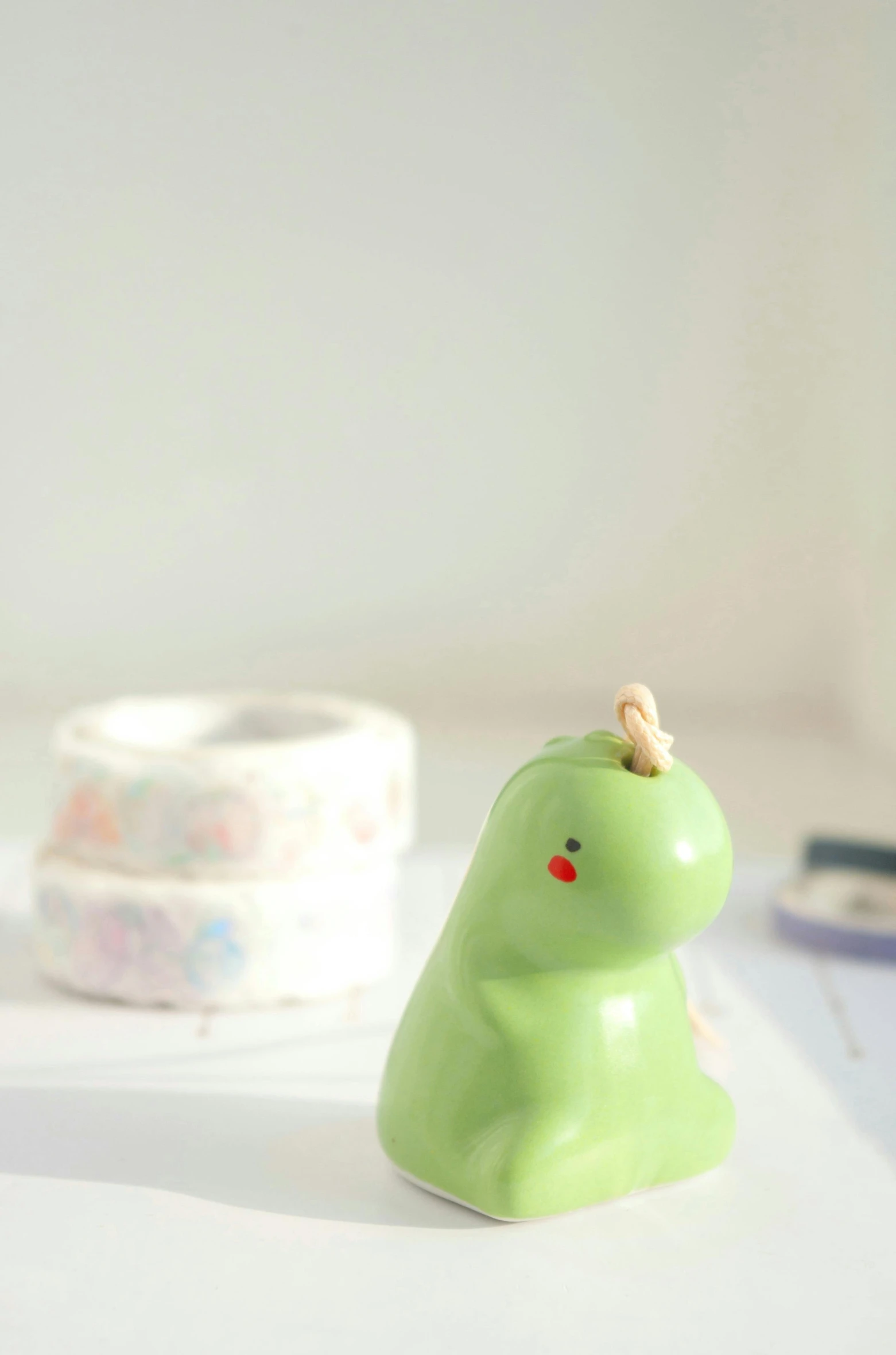 a green toy sitting on top of a table next to a pair of scissors, a picture, by Sylvia Wishart, unsplash, new sculpture, dinosaur wooden statue, pastel glaze, sanrio ornaments, close up shot from the side