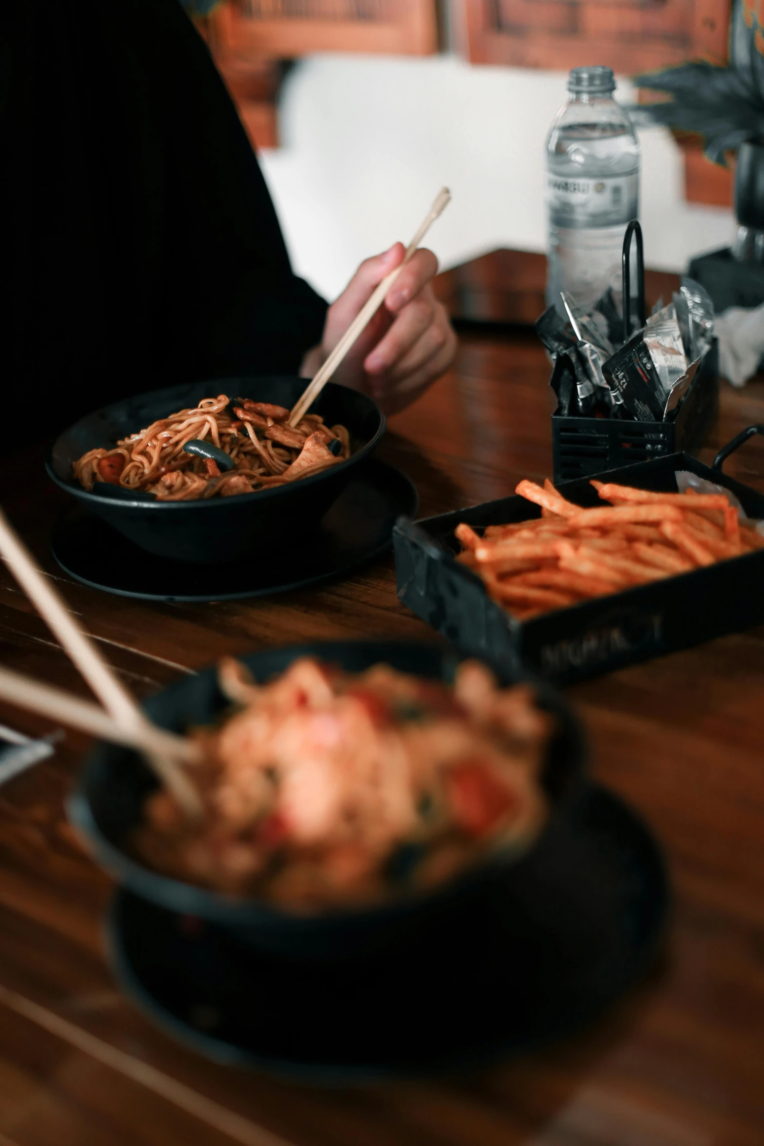 a person sitting at a table with two plates of food, noodles, black fork, wok, high-quality photo