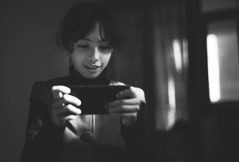 a black and white photo of a woman looking at her cell phone, by Adam Marczyński, finn wolfhard, holding a nintendo switch, mobile game, warm light