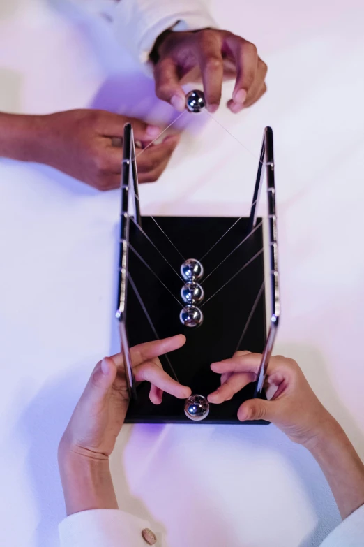 a couple of people that are holding some kind of bag, an abstract sculpture, inspired by Matteo Pérez, trending on reddit, kinetic art, newton's cradle, [ overhead view of a table ]!!, panel of black, with sparkling gems on top