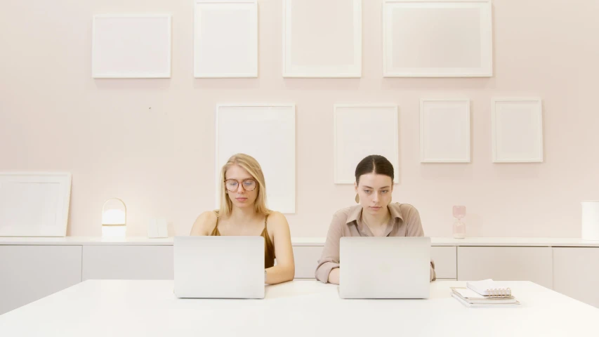 a couple of women sitting at a table with laptops, by Carey Morris, trending on pexels, clean minimalist design, creamy, looking from shoulder, minimal pink palette