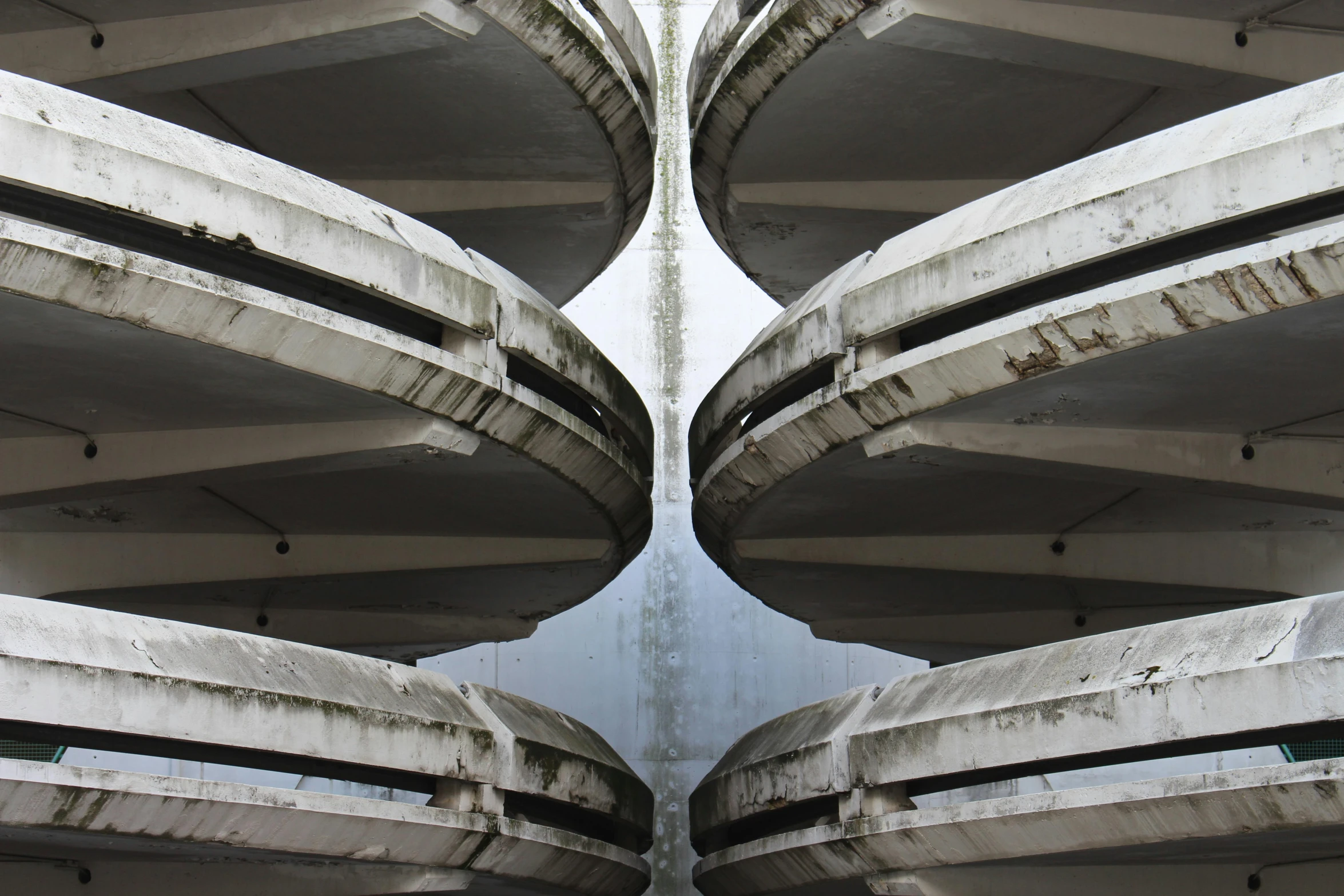 a man riding a skateboard up the side of a building, inspired by Ned M. Seidler, unsplash, brutalism, round doors, cars parked underneath, symmetry fractal, made of concrete