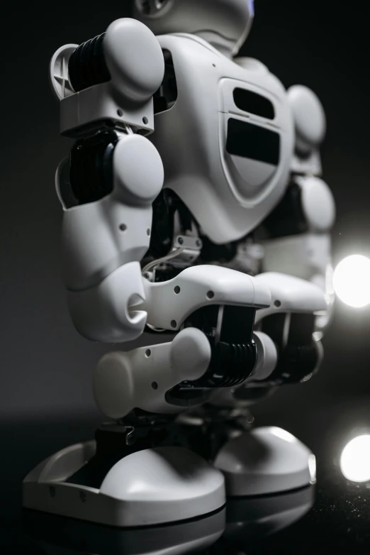 a white robot sitting on top of a table, unsplash, on a black background, close-up of a robot sitting down, ((robot)), low - angle shot