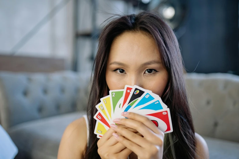 a woman holding a bunch of cards in front of her face, inspired by Aquirax Uno, unsplash, primary colours, young asian girl, game cover, looking left