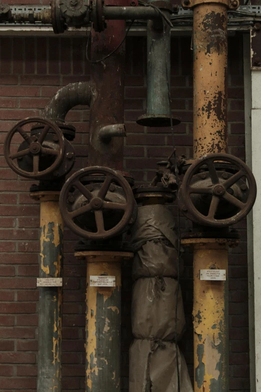 a fire hydrant on the side of a brick building, by Frederik Vermehren, assemblage, industrial rusty pipes, gearwheels, candid photograph, brown