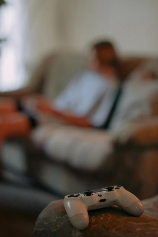 a video game controller sitting on top of a wooden table, a tilt shift photo, by Adam Marczyński, unsplash, elves sitting on the couch, 256435456k film, lounging on expensive sofa, tilt shift suburban