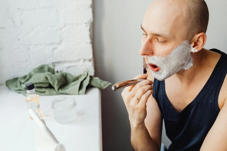 a bald man shaving his face with a razor, by Julia Pishtar, trending on pexels, square masculine jaw, mage smoking pipe, shiny white skin, bearded and built