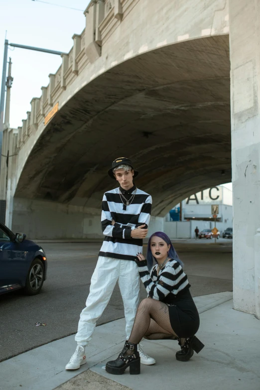 a couple of people standing next to each other on a sidewalk, an album cover, graffiti, an epic non - binary model, sitting under bridge, left eye stripe, white and black clothing