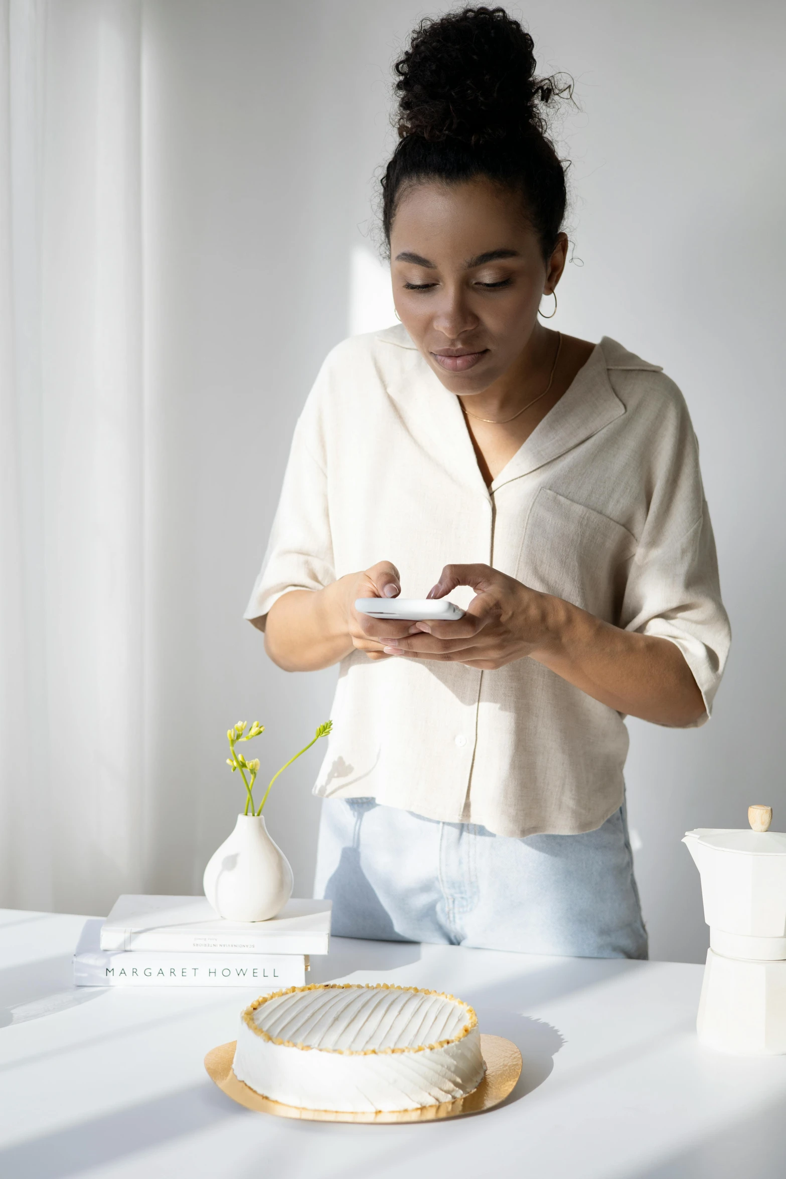 a woman standing in front of a table holding a cell phone, trending on pexels, happening, wearing a linen shirt, reading, samsung smartthings, dwell