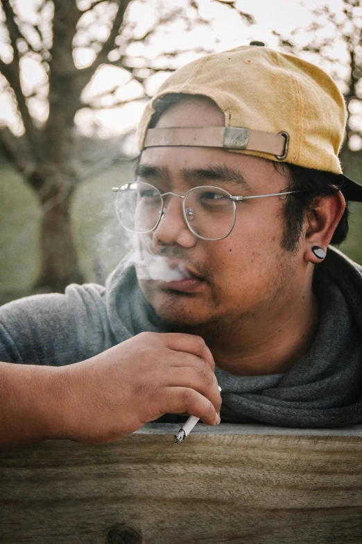 a man sitting on a bench smoking a cigarette, inspired by Eddie Mendoza, unsplash, visual art, wearing small round glasses, halfbody headshot, stoner, 18 years old