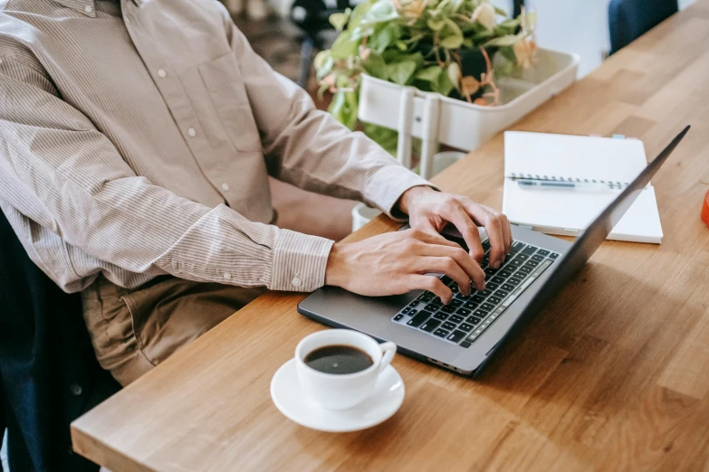 a man sitting at a table using a laptop computer, trending on pexels, sitting on a mocha-colored table, wearing a white button up shirt, thumbnail, a wooden