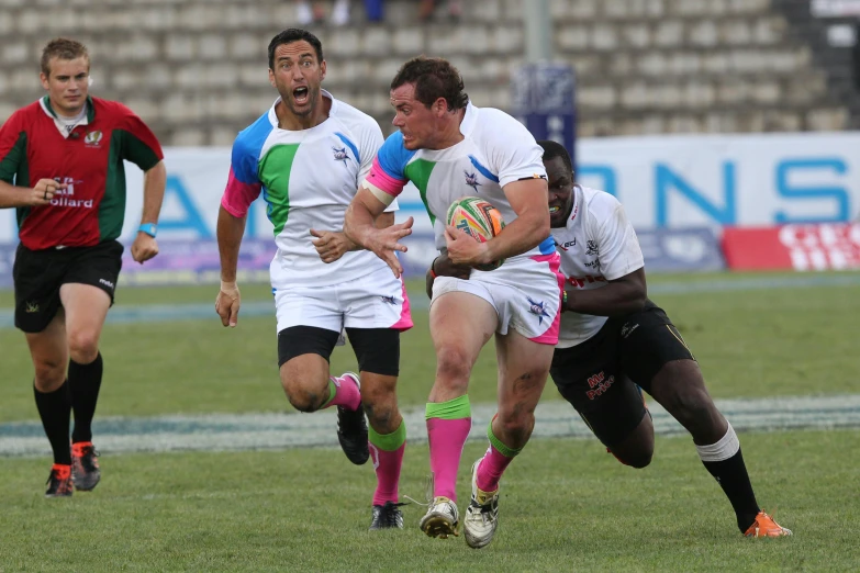 a group of men playing a game of rugby, colorful uniforms, alex kanevsky, pink white turquoise, in a race competition