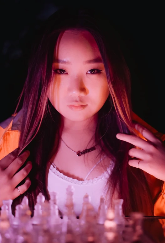 a woman sitting in front of a chess board, an album cover, inspired by Feng Zhu, unsplash, barely lit warm violet red light, looks directly at camera, pokimane, orange glow