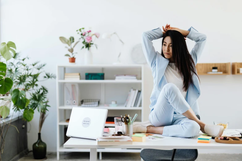 a woman sitting on a desk in front of a laptop, trending on pexels, happening, brunette fairy woman stretching, wearing pajamas, an asian woman, professional comercial vibe