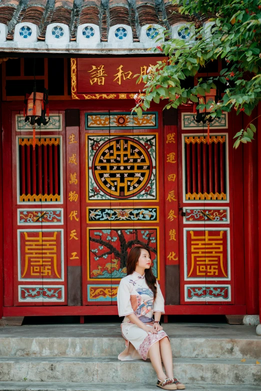 a woman sitting on the steps of a building, a picture, inspired by Luo Mu, pexels contest winner, cloisonnism, massive decorated doors, scarlet and yellow scheme, square, shop front