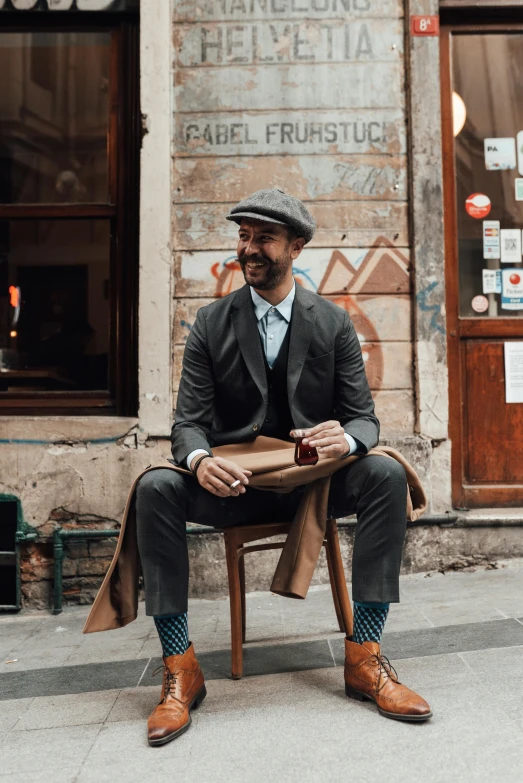 a man sitting on a chair in front of a building, vintage clothing, three piece suit, kreuzberg, thumbnail