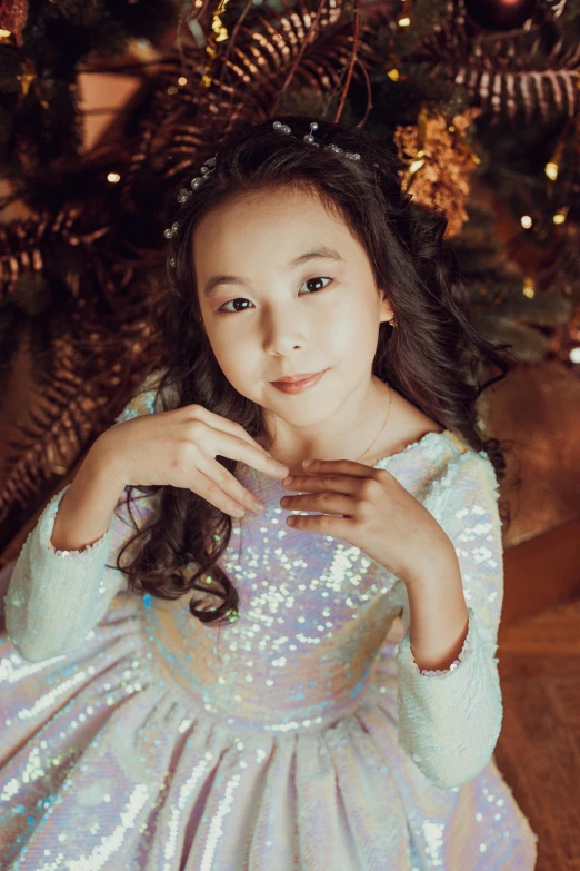 a little girl sitting in front of a christmas tree, an album cover, by Julia Pishtar, pexels contest winner, ao dai, sequins, pearlescent hues, actress